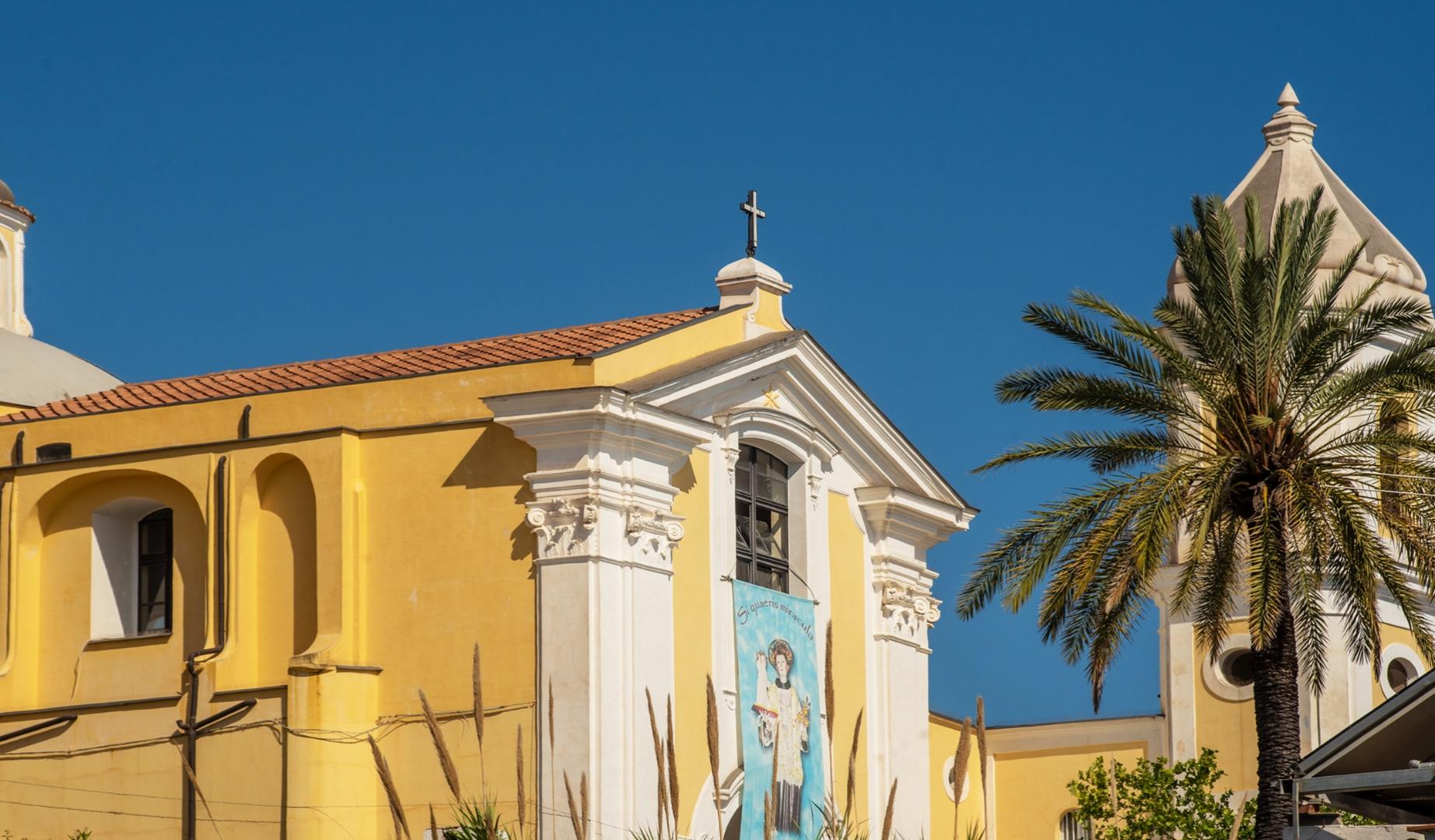 Chiesa gialla con palme, cielo azzurro, atmosfera serena e solare, croce in cima.