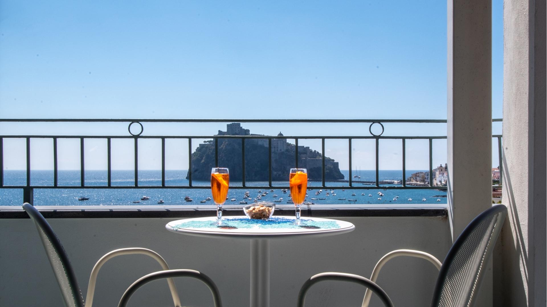 Vista mare con due drink arancioni su tavolo, atmosfera rilassante e romantica.