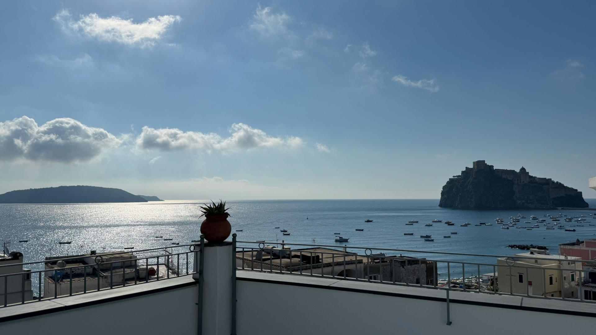 Vista sul mare con isola e barche, cielo azzurro e nuvole soffici.