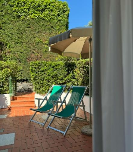 Due sedie a sdraio verdi sotto un ombrellone, circondate da verde lussureggiante e sole.