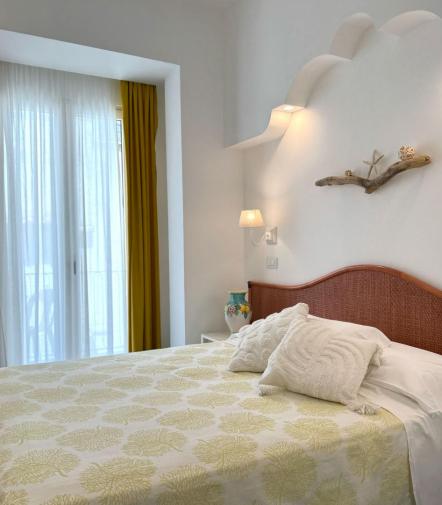 Camera luminosa e accogliente con letto decorato, lampada soffusa e dettagli naturali.