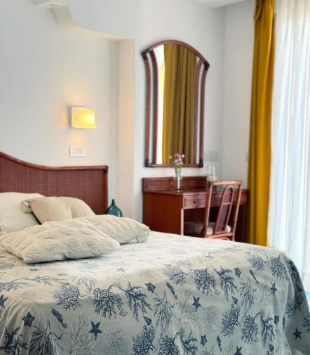 Camera luminosa con letto accogliente, specchio elegante e tende gialle vibranti.