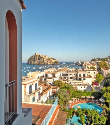 Vista su un castello sul mare, case bianche, piscina, atmosfera mediterranea e cielo limpido.
