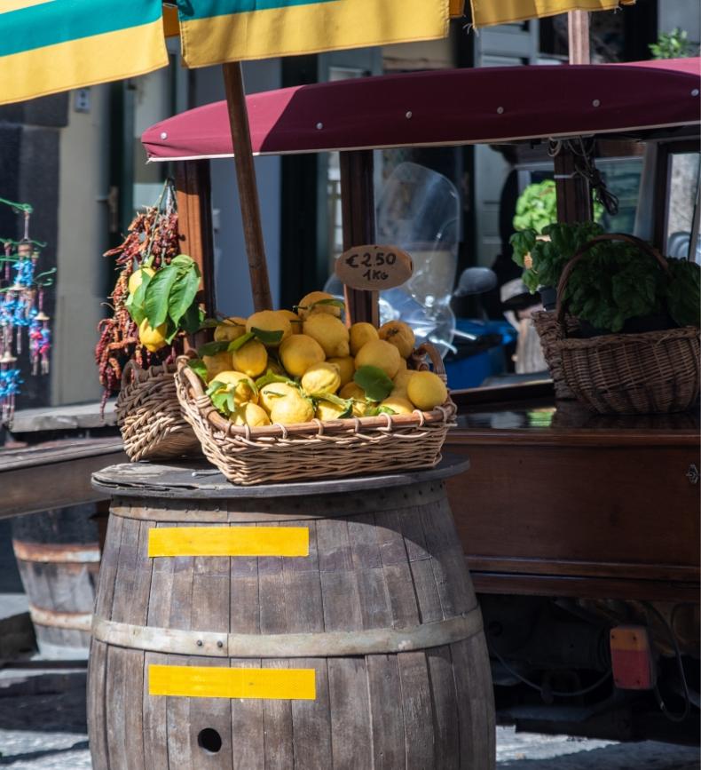 Cesto di limoni su botte di legno, sotto un ombrellone colorato, in un mercato vivace.