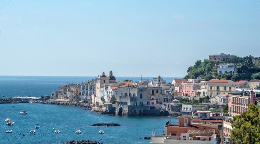 Vista costiera idilliaca con case colorate, mare blu e barche galleggianti, atmosfera serena e pittoresca.