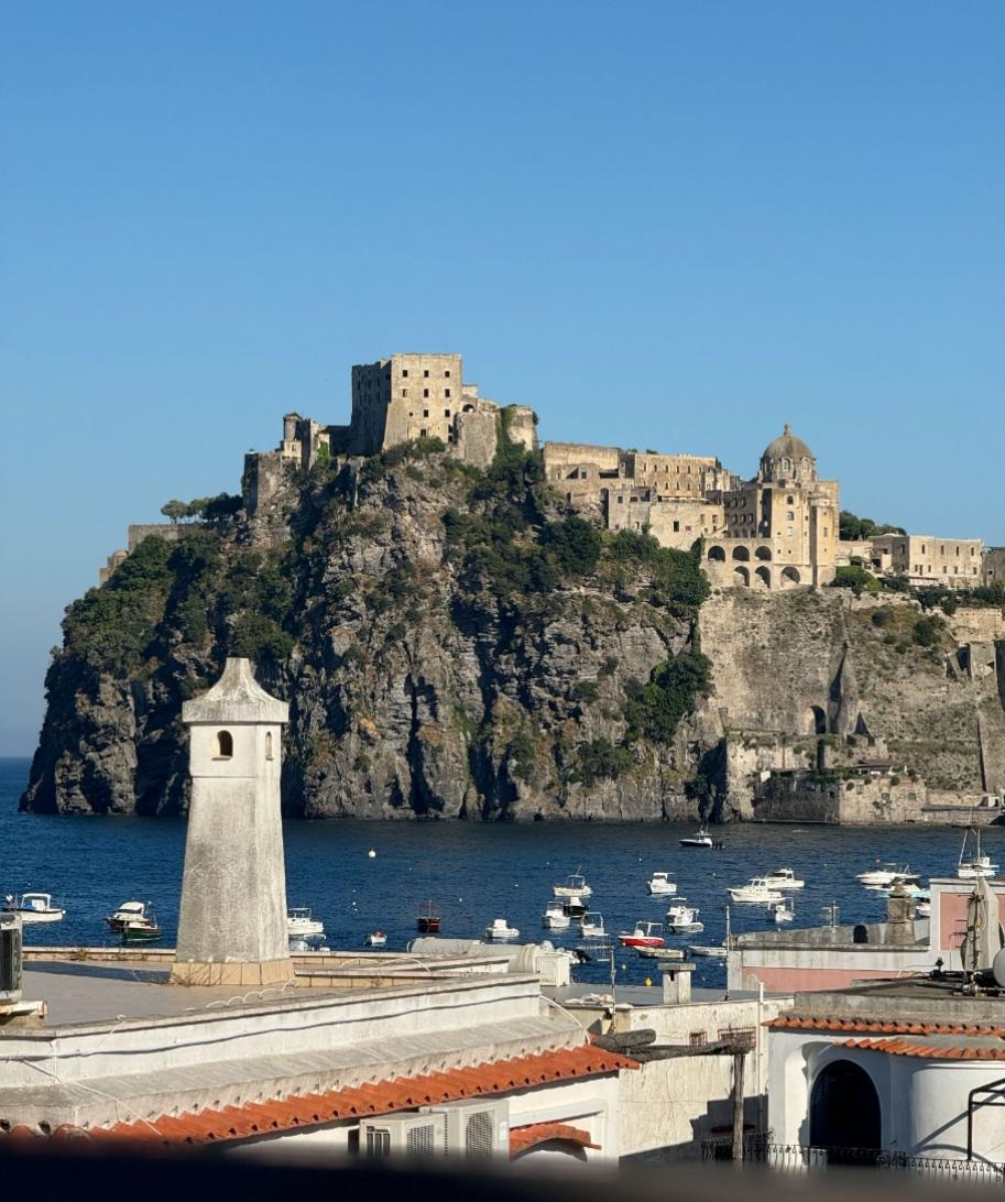 Imponente castello su scogliera, mare blu, barche, cielo limpido: un quadro di serenità.